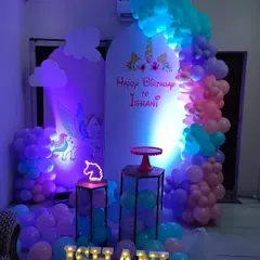 This enchanting unicorn theme uses moody lighting to create a magical effect. The setup includes a winged unicorn backdrop, a pastel balloon arch, and light-up props like a unicorn neon sign and the birthday girl's name.