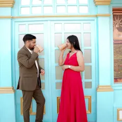 A playful moment sharing a drink against a vibrant blue door, reminiscent of a European street. The woman's bright red dress pops against the cool tones, creating a lively and stylish pre-wedding photo.