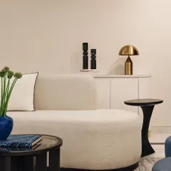 This living area is filled with warm tones and inviting textures. The space features a comfortable curved sofa, a sculptural black side table, and a fluted white console, creating a harmonious blend of modern shapes and soft materials.