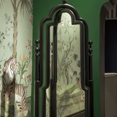 A freestanding mirror from our House of Goya line, featuring a traditional carved black frame. It reflects a vibrant, tropical wallpaper, showing how our furniture pieces can complement a variety of bold interior styles.