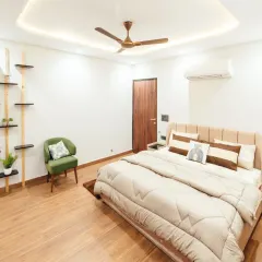 A spacious and airy bedroom design with light wood flooring and white walls. The minimalist shelving and a pop of color from the green armchair create a clean yet inviting look.
