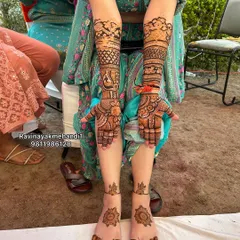 A beautiful shot of a bride showcasing her full hand and foot mehndi. The arm design features classic peacock and floral work, while the feet have elegant mandala patterns.