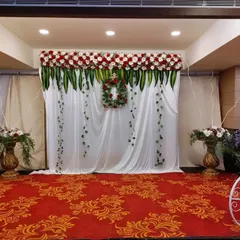 A chic and modern engagement backdrop with a white curtain, a floral wreath, and arrangements of red and white roses. The white bicycle prop adds a whimsical touch.