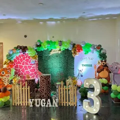 A vibrant jungle safari theme, perfect for a wild third birthday party. This setup features a lush green backdrop, fun animal cutouts like a tiger and elephant, a large light-up marquee number '3', and custom plinths with animal prints.