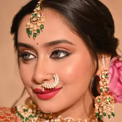 A close-up of a modern traditional look. The makeup features sharp winged eyeliner and a bold pink lip, with a lotus flower in the hair for a unique touch.