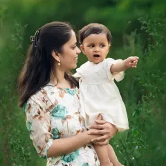 A mother holds her baby girl, who is pointing at something with wonder. This candid moment was captured during a beautiful outdoor sitter session.
