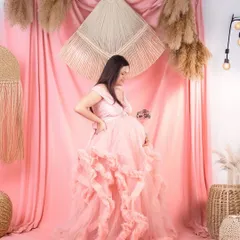 Pretty in pink. This mom-to-be is glowing in a pastel pink gown with a uniquely textured ruffled skirt, set against a matching bohemian-inspired studio backdrop.