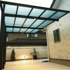 This modern carport features a translucent polycarbonate roof and a minimalist black frame. The design provides shelter for the vehicle while allowing light to pass through, preventing the area from feeling dark.