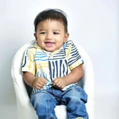 A happy, smiling portrait of one of the twin boys. Using a simple white chair and background keeps the focus entirely on his joyful expression.