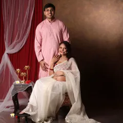 A beautiful couple portrait in traditional attire. The mom-to-be glows in a sheer white saree, her bump visible, creating a modern yet traditional look.