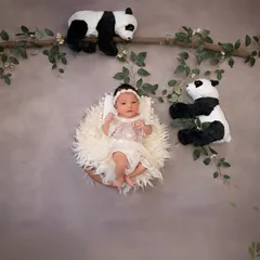 An adorable awake moment in a whimsical panda-themed setup. The baby is nestled in a fluffy basket against a neutral backdrop, surrounded by playful pandas climbing on branches.