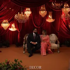 A candid moment of the couple on their beautifully designed reception stage. The warm glow of the chandeliers and the rich red backdrop create a picture perfect setting for their celebration.