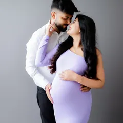 A stylish and modern couple's portrait. The mom-to-be looks radiant in a lavender bodycon dress, sharing a loving gaze with her partner against a clean, simple backdrop.
