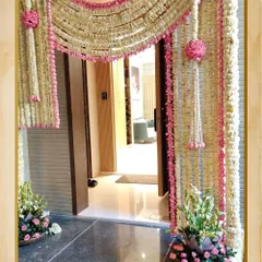 A traditional and dense floral entrance for a home. This arch is made with rajnigandha (tuberose) and pink rose garlands, creating a beautiful and fragrant welcome for guests.