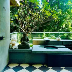 A stunning balcony water feature in Swami Nagar, Delhi. The design includes a gentle fountain, a Buddha statue for serenity, and a beautiful Frangipani tree, all set against a backdrop of lush greenery.