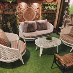 A classic white wicker sofa set that exudes elegance. The set includes a two-seater sofa and two armchairs with intricate woven details, complemented by striped cushions. Placed in a lush green setting with decorative elements, it shows how our furniture can create a timeless and sophisticated outdoor parlor.