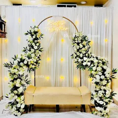 A modern and chic Roka setup with a golden ring arch, asymmetrical white floral arrangements, and a 'Better Together' neon sign against a fairy light backdrop.