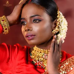A close-up portrait showcasing the artistry of South Indian bridal styling. The focus is on the traditional jasmine flowers in the hair, the gold jhumkas, and the dramatic eye makeup.