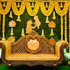 A budget-friendly baby shower backdrop using a wall of green leaves, marigold garlands, and a cutout of a mother and child, creating a sweet and simple photo point.