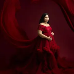 A dramatic and elegant solo maternity portrait. The flowing red gown and rich backdrop create a powerful, artistic image that celebrates the beauty of pregnancy.