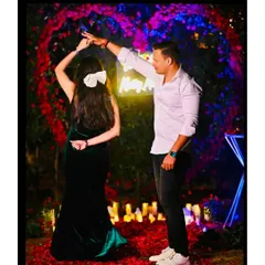 The newly engaged couple sharing a dance. The ambient lighting from the candles and the floral heart arch creates a dreamy, cinematic feel.
