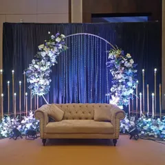 A modern and chic reception stage featuring a circular arch with blue and white florals and elegant crystal hangings.