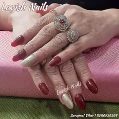 A stunning combination of deep red and shimmering gold accent nails, accessorized with statement rings for a complete, glamorous look.