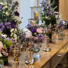 An elegant console table arrangement featuring a mix of purple and white blossoms with modern glass and gold candle holders. This style of decor adds a touch of sophistication to any corporate lobby or event space.