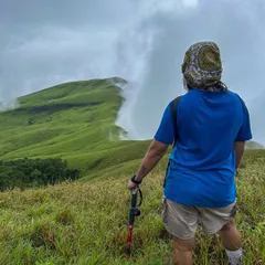A trekker with a walking pole gazes at the "wall of clouds" approaching the Netravathi trail. This is what trekking in the Western Ghats is all about.