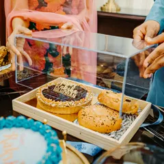 This is one of my signature Rakhi hampers, presented in a modern acrylic and wood tray. It includes a mix of sweet and savoury treats like a 'Happy Raksha Bandhan' tart and freshly baked bagels.