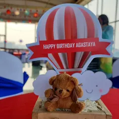 A close-up of a table centerpiece featuring a cute teddy bear sitting in front of a red and white striped hot air balloon cutout. These little details make the theme come alive on every table.