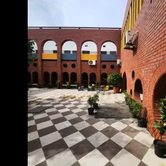 The refurbished internal courtyard of a primary school, featuring a facade of brick arches and a checkered floor. The open, airy space is designed to be a central hub for play and interaction.