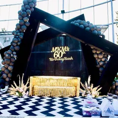 This was the central photo-op for a 60th birthday bash. We designed a modern, geometric black backdrop with custom gold lettering, a shimmering gold fringe sofa, and balloon garlands for a perfectly stylish picture spot.