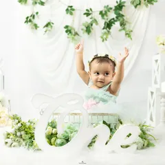A beautiful first birthday portrait. This baby girl celebrates turning one in a whimsical setup with white and green floral decorations.