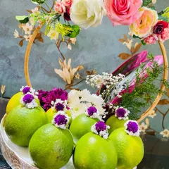 I love using fresh, natural elements in my designs. This tray features a ring of vibrant green lemons, each topped with a small purple flower, surrounding a central bouquet. It's a unique and refreshing take on a traditional fruit tray.