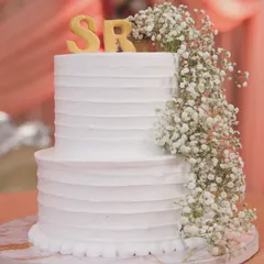 A classic two-tiered white wedding cake with a textured buttercream finish. It's personalized with the couple's initials "SR" and a cascading arrangement of fresh baby's breath for a timeless look.