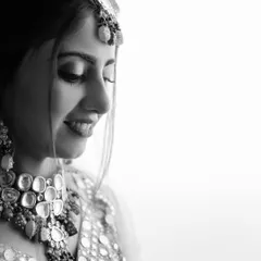 A moment of quiet joy captured in classic black and white. This portrait highlights the bride's beautiful smile and the intricate details of her mirror-work jewelry, creating a timeless and artistic image.