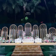 This magnificent outdoor stage is designed for a grand statement, with towering gold birdcage-inspired structures, lush pastel florals, and a dramatic staircase entrance.