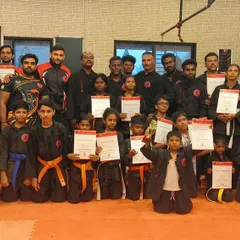 A proud group of students, both children and adults, holding up their new certificates after a successful belt grading.