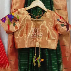 A close-up of the Paithani blouse. The golden tissue silk fabric has colorful, woven parrot and floral motifs on the puff sleeves, a signature of Paithani weaving.