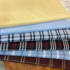 A selection of my premium cotton fabrics for custom shirts. This stack includes classic gingham, tartan, and other check patterns in various colors.