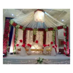 This wedding mandap setup combines traditional red and white florals with a canopy of sheer fabric and lights. The result is a vibrant and sacred space for the wedding ceremony, blending tradition with modern elegance.