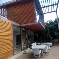 A daytime view of our modern villa project highlights the clean lines and material palette. The combination of wood cladding, a robust steel pergola, and an expansive deck creates a functional and elegant outdoor living area.