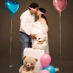 A playful and sweet gender reveal concept. The blindfolded couple, surrounded by pink and blue balloons and teddy bears, builds anticipation for the big surprise.