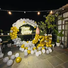 An elegant 25th birthday party on a terrace. The decor features a white and gold circular balloon arch, a neon sign, and matching foil balloons for the age.