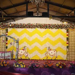 A large-scale floral backdrop for a Sreemantham with a yellow and white chevron pattern made of fresh flowers. The stage includes a decorated cradle and cow motifs for a traditional touch.