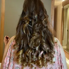 A beautiful view of this half-up, half-down hairstyle. The hair is styled in defined, bouncy curls with a delicate pearl chain accessory for a touch of elegance.