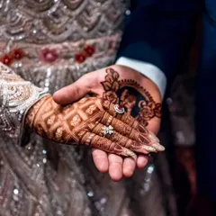 A unique detail shot showing the bride's mehndi-adorned hand in the groom's, which features a custom henna portrait of the bride.