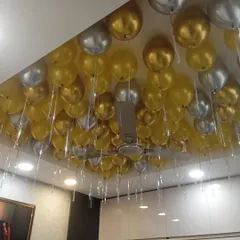 To make a room feel full and festive, I can decorate the entire ceiling with balloons. Here, I used gold and silver balloons with hanging ribbons to cover the ceiling for a party.