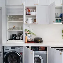 In this all-white kitchen, the washing machines are hidden behind cabinet doors, completely disappearing into the design. This allows the space to maintain its serene and uncluttered look while still being highly functional.